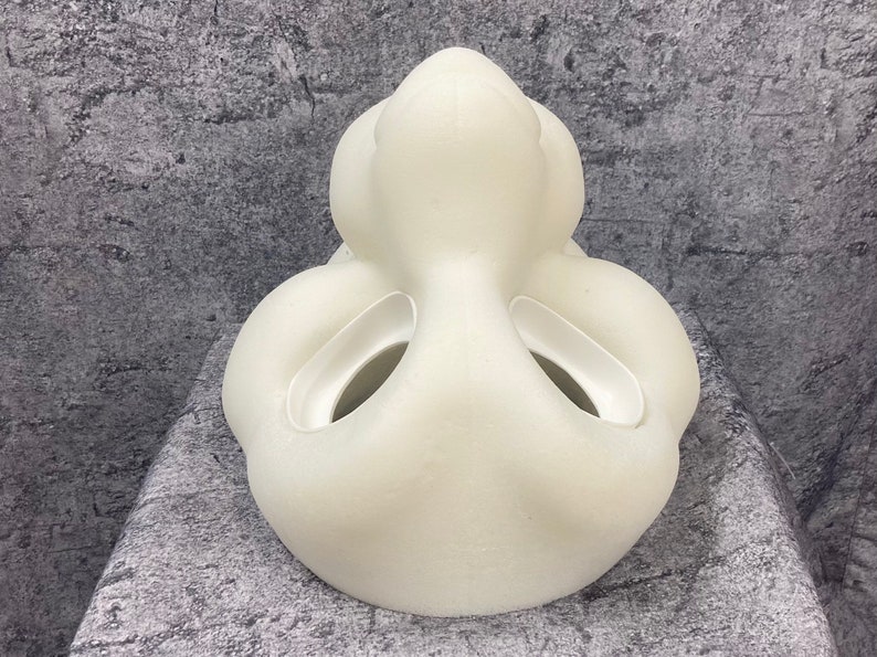 K&ouml;nnte beinhalten: Eine wei&szlig;e, glatte, 3D-gedruckte Maske mit zwei gro&szlig;en L&ouml;chern an den Seiten und einem kleineren Loch in der Mitte. Die Maske ist so konzipiert, dass sie einem Gesicht &auml;hnelt.
