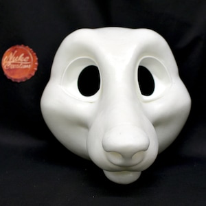 Könnte beinhalten: Weiße, unfertige Felltiermaske mit großen Augenlöchern und einer großen Nase. Die Maske besteht aus einem glatten, harten Material.