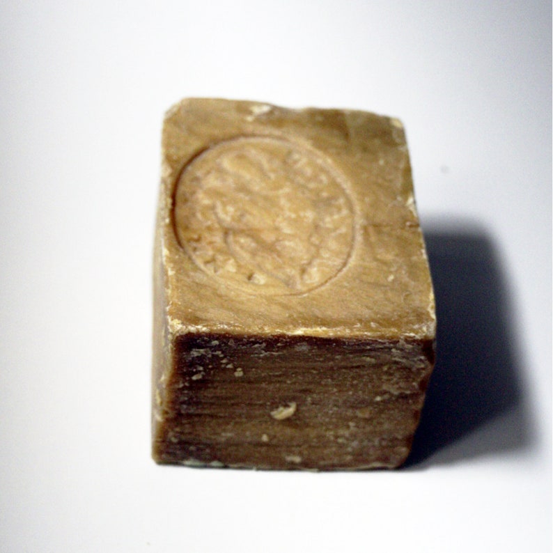 May include: A rectangular bar of brown soap with a raised circular design on the top. The design features a stylized image of a person's head.