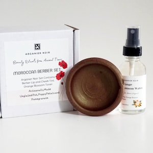 Puede incluir: Un set de belleza bereber marroquí con una pequeña maceta de terracota sin esmaltar, una botella de agua de azahar y una caja con el texto "Arganier Noir Beauty Rituals from Ancient Times Moroccan Berber Set".