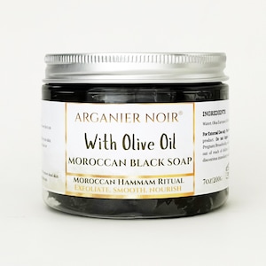 May include: A clear plastic jar filled with dark Moroccan black soap, topped with a silver screw-on lid. The white label features the text Arganier Noir, With Olive Oil, Moroccan Black Soap, Moroccan Hammam Ritual, and 7oz/200g.