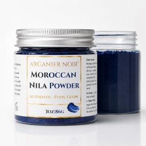 May include: A clear plastic jar with a silver lid containing deep blue Moroccan Nila Powder. The white label features the text Arganier Noir, Moroccan Nila Powder, Authentic. Even. Glow, and 3oz|86g, along with usage instructions for face and body.