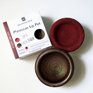 May include: Two terracotta pots containing Moroccan lip and cheek stain. The pots are labeled "Moroccan Lip Pot" and "Lip & Cheek Stain". The packaging is white with black text and a red heart.