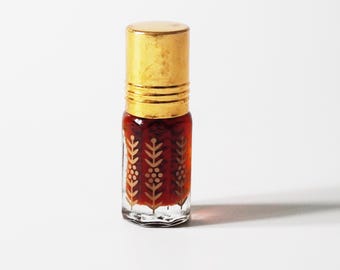May include: A small glass perfume bottle with a gold cap and gold leaf design. The bottle is filled with a dark red liquid. The bottle is on a white background.