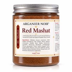 May include: A clear glass jar filled with reddish-brown herbal powder, topped with a silver metal lid. The label reads Arganier Noir Red Mashat, listing ingredients like Shikakai, Amla, and Sidr, with a net weight of 142g or 5oz printed on the front.