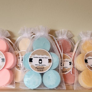 Puede incluir: Varias velas peque&ntilde;as y redondas de cera de soja perfumada en bolsas de organza. Las velas son de varios colores, incluyendo rosa, azul y amarillo. Cada bolsa tiene una etiqueta con el texto "Candles by Jess Bean" y un nombre de aroma.