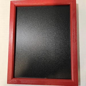 May include: A rectangular chalkboard with a red wooden frame. The chalkboard has a textured black surface. The frame is painted red and has visible wood grain.