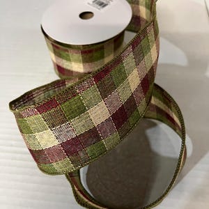May include: A roll of decorative ribbon with a plaid pattern in shades of green, burgundy, and beige. The ribbon is made of a woven material and is ideal for crafts, gift wrapping, or seasonal decorations.