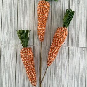 May include: Three orange and white striped carrot decorations with green leafy tops.