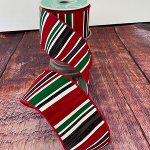 May include: Red, white, black, and green striped ribbon with a wired edge. The ribbon is on a spool and is ready to be used for crafting or decorating.