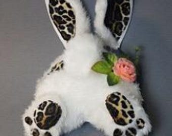 May include: White plush bunny rabbit with leopard print ears, paws, and accents. The bunny has a pink flower on its back.