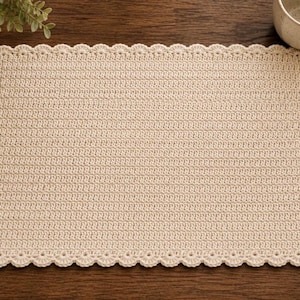May include: A rectangular cream-colored crochet placemat featuring a dense, uniform stitch pattern throughout the center and a decorative scalloped edge border that frames the entire perimeter of the textile piece.