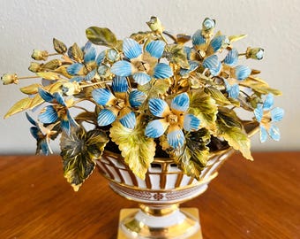 May include: A gold-plated ceramic vase with a white base and gold trim, holding a bouquet of blue and gold metal flowers.