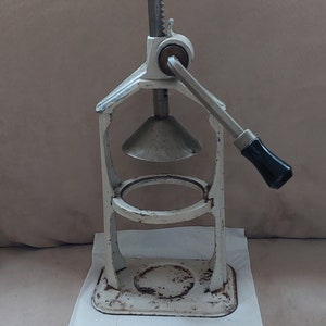 May include: White metal citrus press with a black handle and a cone-shaped juicer. The press is on a white paper napkin.