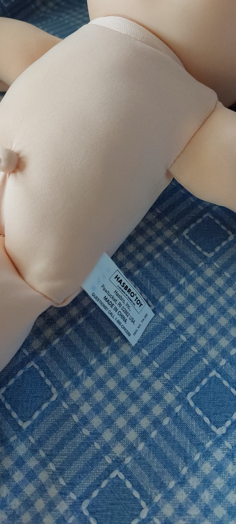 K&ouml;nnte beinhalten: Eine wei&szlig;e Puppe mit einem Hasbro Toy-Etikett mit der Aufschrift "Hasbro, Inc., Pawtucket, RI 02862 USA. MADE IN CHINA. QUESTIONS? CALL 1-800-CPKIDSS"