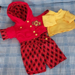May include: A red hooded jacket with yellow buttons, a black and red diamond pattern on the cuffs and lining, and a yellow and red patch with the letters CPK. Beside it is a plain yellow long-sleeved shirt and red trousers with a black diamond pattern.