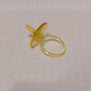 Puede incluir: Un chupete de bebé de plástico amarillo con un asa de anillo.