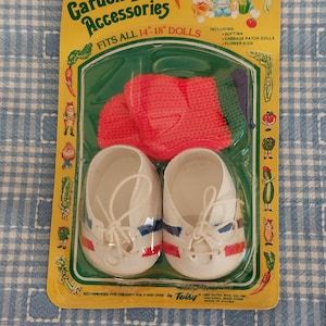 May include: A vintage Garden Doll Accessories set, including shoes, a sweater, and other accessories. The packaging is yellow and green, with the text "Garden Doll Accessories" and "Fits All 35.5-45.7 cm Dolls". The set includes white shoes with red and blue stripes.