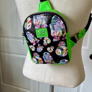 May include: A small, black and green backpack with a colorful Star Wars character print. The bag features a bright green trim and strap, with the text "calm your knits" on a green patch.