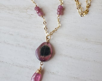 May include: A gold chain necklace with a pink and black gemstone pendant and pink gemstone accents.