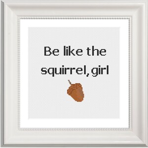 May include: White framed cross-stitch with the text "Be like the squirrel, girl" and a brown acorn in the center.