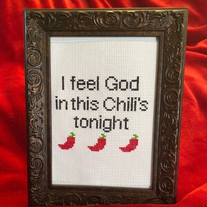 May include: A framed cross-stitch with the text "I feel God in this Chili's tonight" and three red chili peppers.