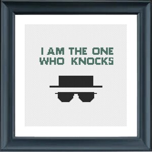 May include: A framed cross-stitch design featuring the text "I am the one who knocks" and a black silhouette of a man wearing a hat and sunglasses. The text is in green.