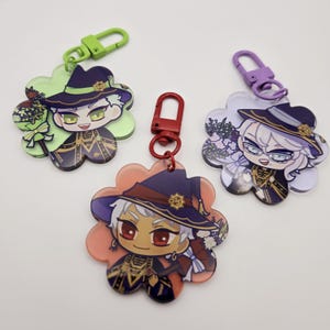 May include: Three flower-shaped keychains with different colored backgrounds. Each keychain features a cartoon character wearing a witch's hat and holding a staff. The characters have different colored hair and skin tones.