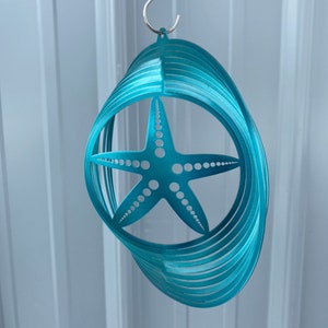 May include: Teal blue metal wind spinner with a starfish design. The spinner is hanging from a silver chain.