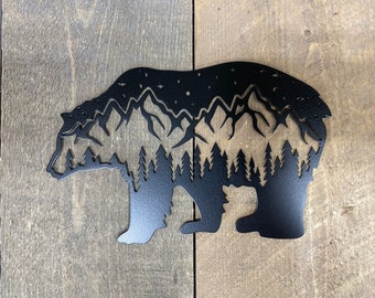 May include: Black metal silhouette of a bear with a mountain range and forest inside. The bear is standing on a wood background.