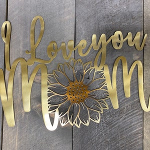 May include: Gold metal wall art with the words "Love you Mom" and a sunflower design.