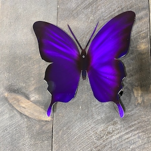 May include: A purple metal butterfly wall decor with a gradient effect. The butterfly is made of metal and has a shiny finish.