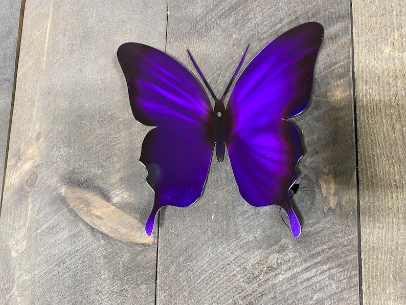 May include: A purple metal butterfly wall decor with a gradient effect. The butterfly is made of metal and has a shiny finish.
