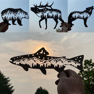 May include: A set of five black paper cutouts of animals and a fish, each with a mountain range and trees inside. The animals include a bear, an elk, a wolf, and a fish.