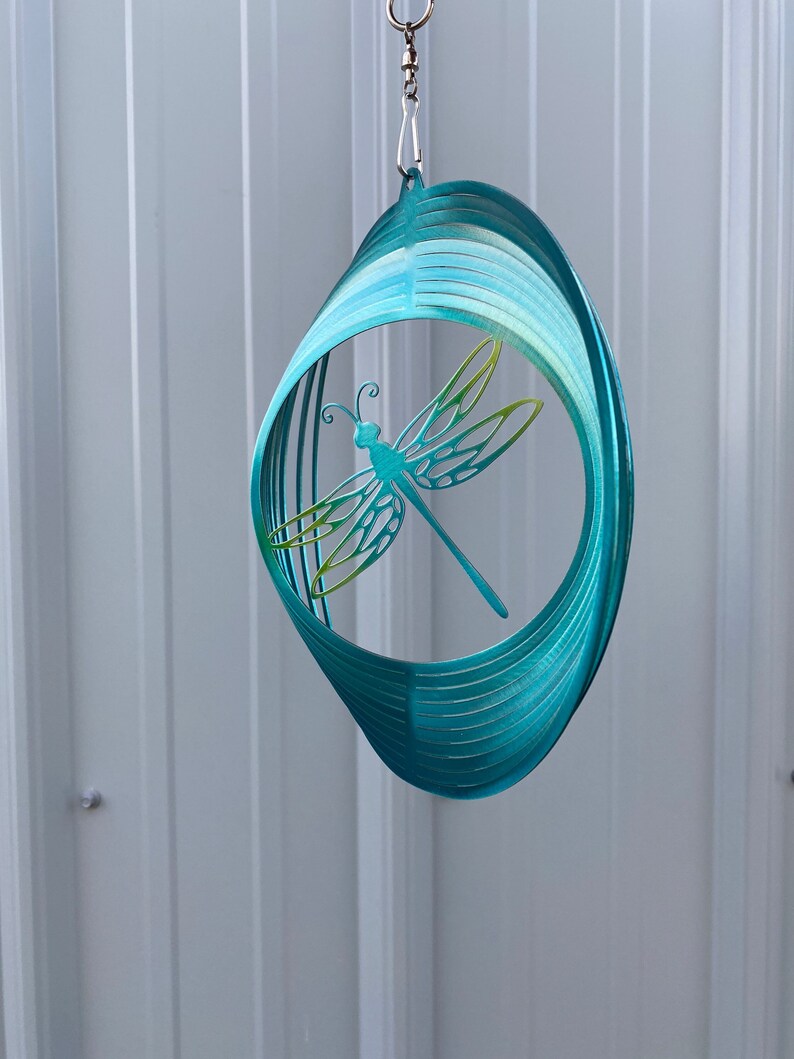 May include: A teal blue metal wind spinner with a dragonfly design. The dragonfly is cut out of the metal and has a green and yellow colour gradient.