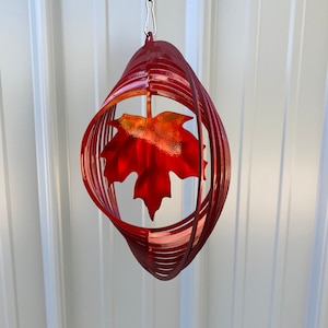 May include: Red metal wind spinner with a red maple leaf design. The spinner is suspended from a silver chain.