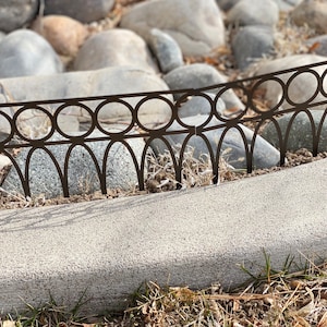 May include: A brown metal garden edging with a decorative design of circles and arches. The edging is broken in one spot.