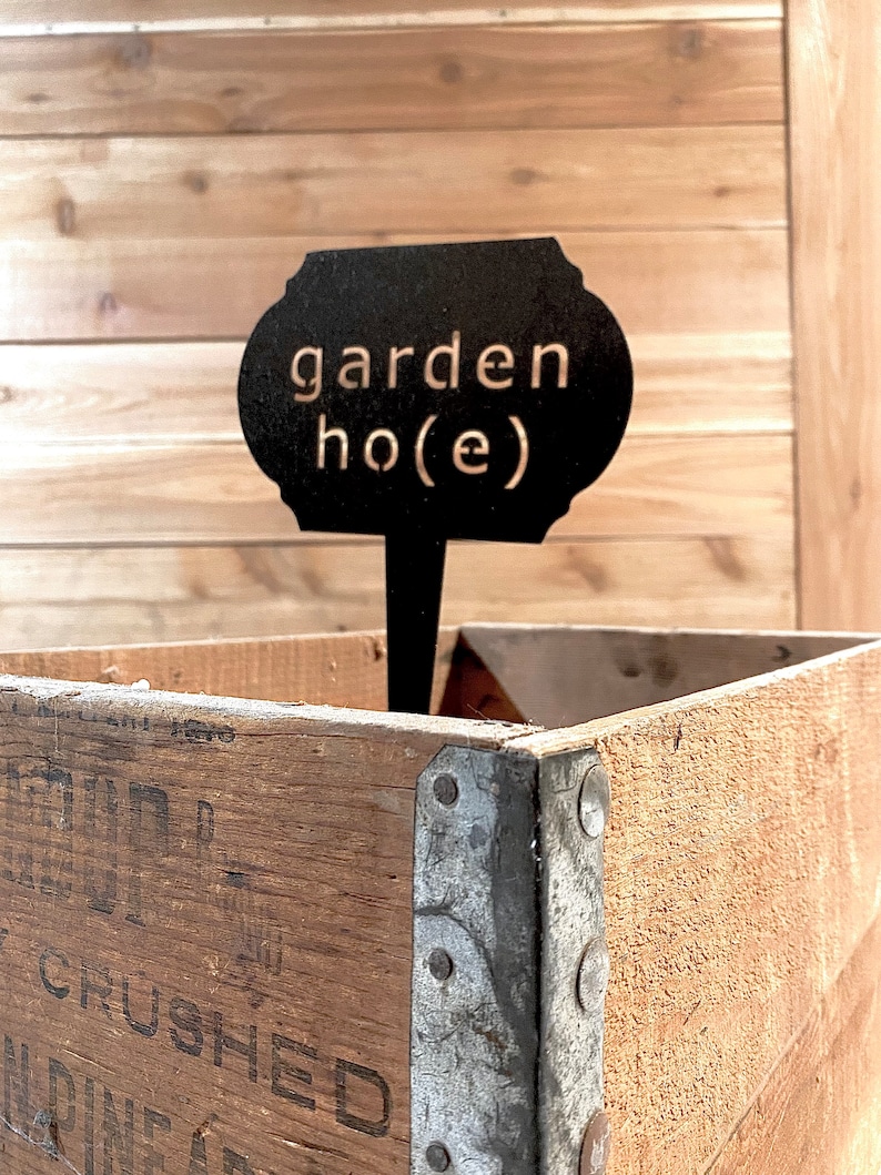 May include: Black metal garden marker with the text "garden ho(e)" in white lettering. The marker is inserted into a wooden crate.