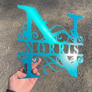 以下が含まれることがあります： ターコイズブルーの金属製のモノグラムで、Nの文字とNORRISという名前が装飾的なフォントで書かれています。モノグラムは切り抜かれており、光沢のある仕上げになっています。