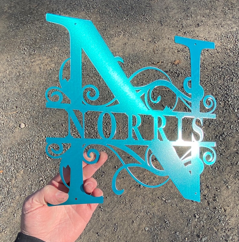 以下が含まれることがあります： ターコイズブルーの金属製のモノグラムで、Nの文字とNORRISという名前が装飾的なフォントで書かれています。モノグラムは切り抜かれており、光沢のある仕上げになっています。