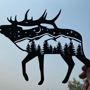 Op de afbeelding: Zwarte papieren uitsnijding van een eland met een bergketen en sterren in de silhouet.