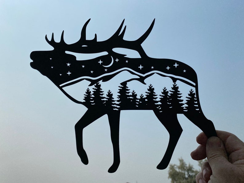 Op de afbeelding: Zwarte papieren uitsnijding van een eland met een bergketen en sterren in de silhouet.