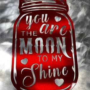 May include: Red metal mason jar shaped sign with the text "You are the moon to my shine" and three silver hearts.