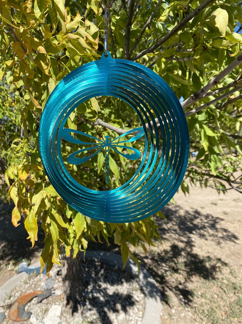 May include: Teal metal wind spinner with a dragonfly design. The spinner has multiple layers of metal that create a swirling effect when it spins in the wind.