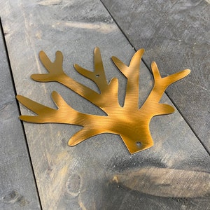 Puede incluir: Una decoraci&oacute;n de pared de rama de &aacute;rbol de metal dorado con acabado cepillado. La rama est&aacute; hecha de metal y tiene un aspecto r&uacute;stico.