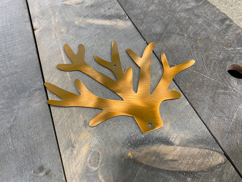 Puede incluir: Una decoraci&oacute;n de pared de rama de &aacute;rbol de metal dorado con acabado cepillado. La rama est&aacute; hecha de metal y tiene un aspecto r&uacute;stico.