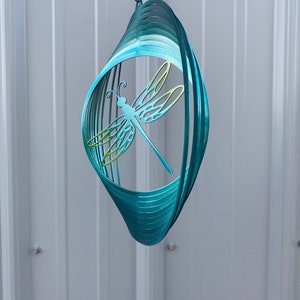 May include: A teal blue metal dragonfly wind spinner with a swirling design. The dragonfly is cut out of the metal and has a green and yellow gradient.