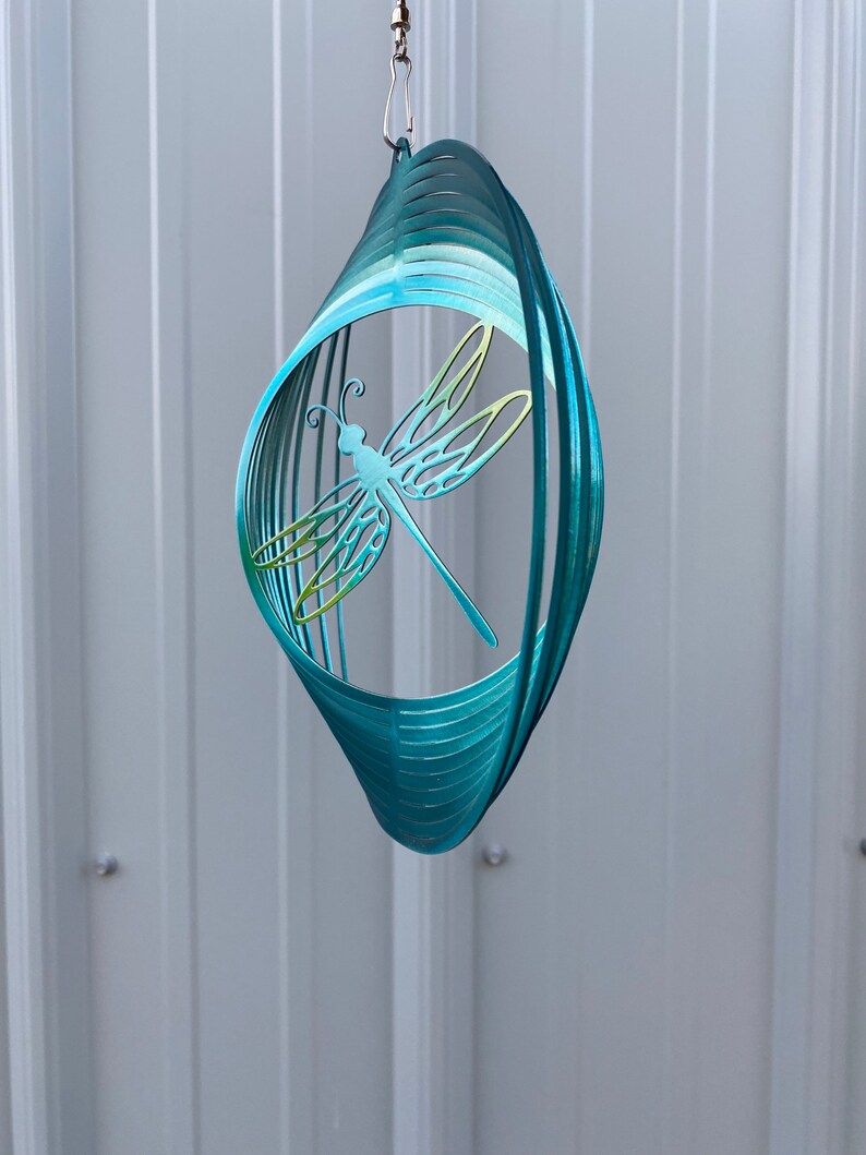 May include: A teal blue metal dragonfly wind spinner with a swirling design. The dragonfly is cut out of the metal and has a green and yellow gradient.