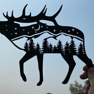 Op de afbeelding: Zwarte papieren uitsnijding van een eland met een bergketen en een sterrenhemel binnen de silhouet.