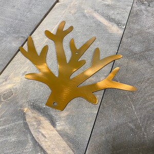 Puede incluir: Un recorte de metal dorado de una rama de &aacute;rbol estilizada con m&uacute;ltiples ramas. El recorte est&aacute; sobre una superficie de madera gris.